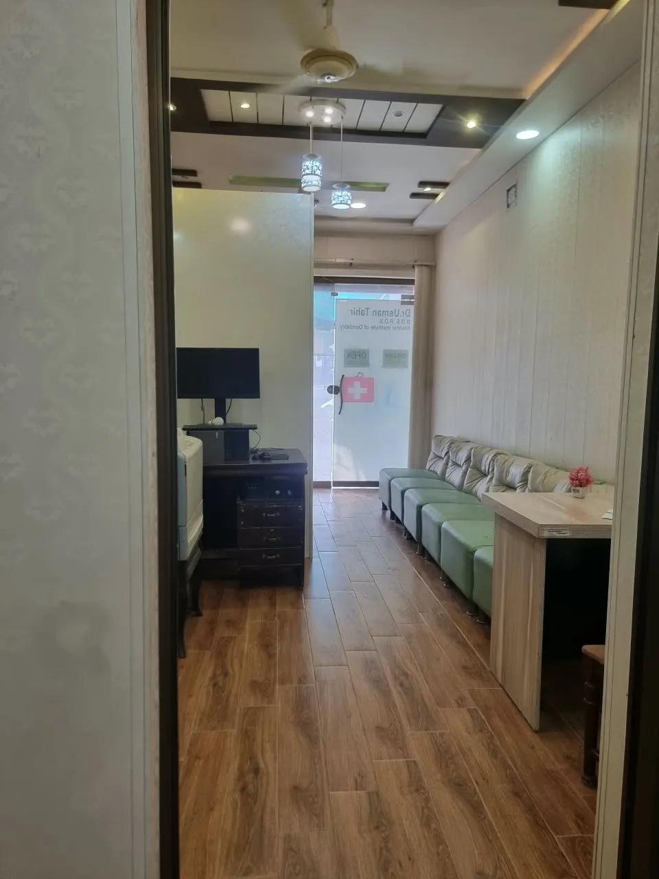 Entrance and reception area of Al-Rehman Dental Care with a glass front door, reception desk and green seating